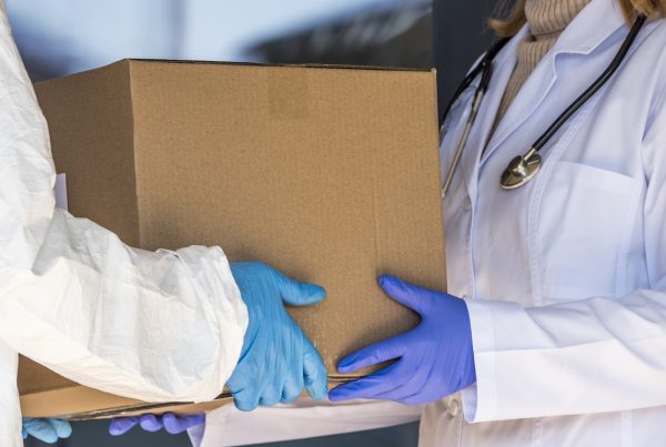 one person in a lab coat hands pharmaceutical packaging to another