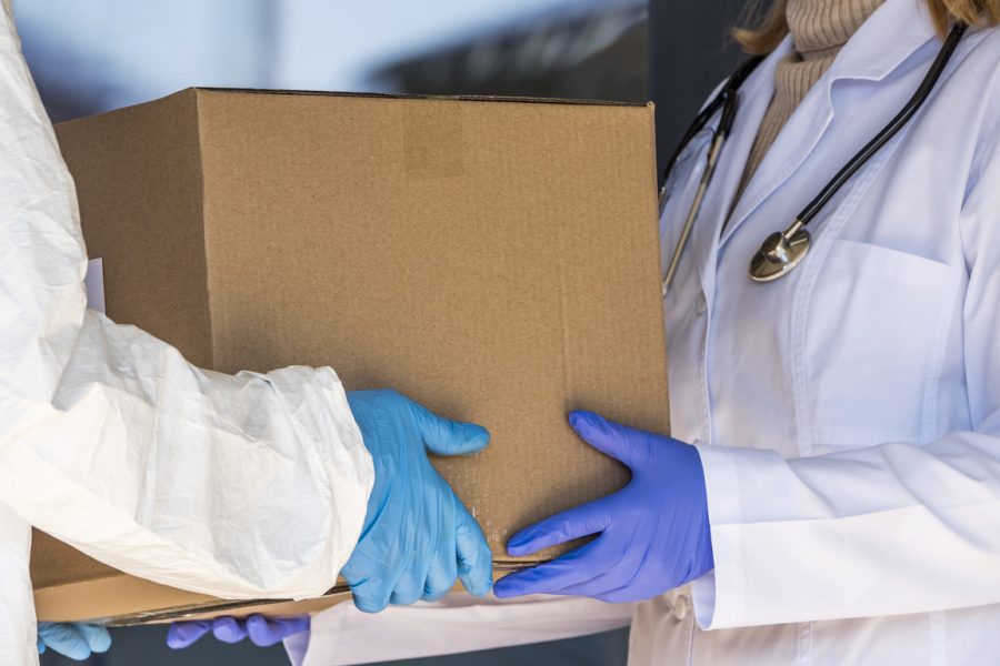 one person in a lab coat hands pharmaceutical packaging to another