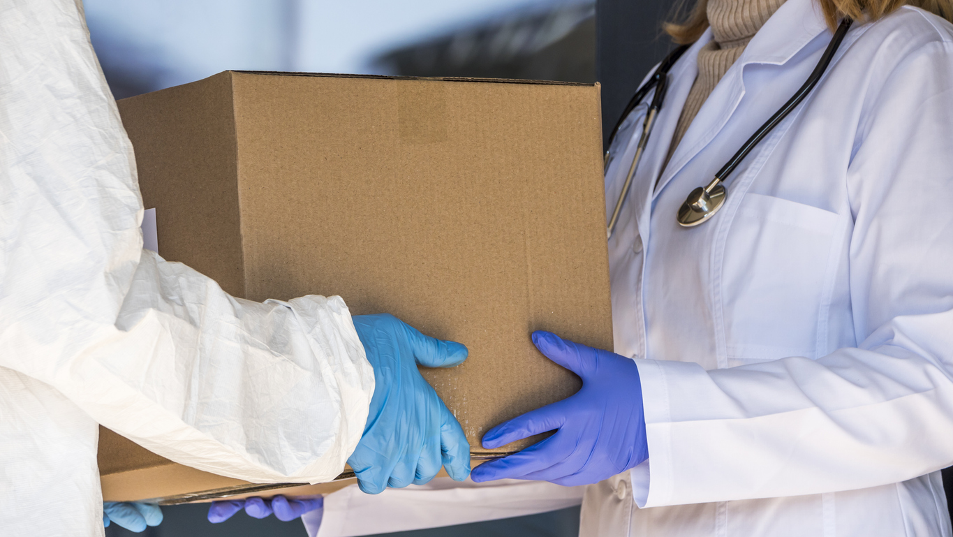 one person in a lab coat hands pharmaceutical packaging to another